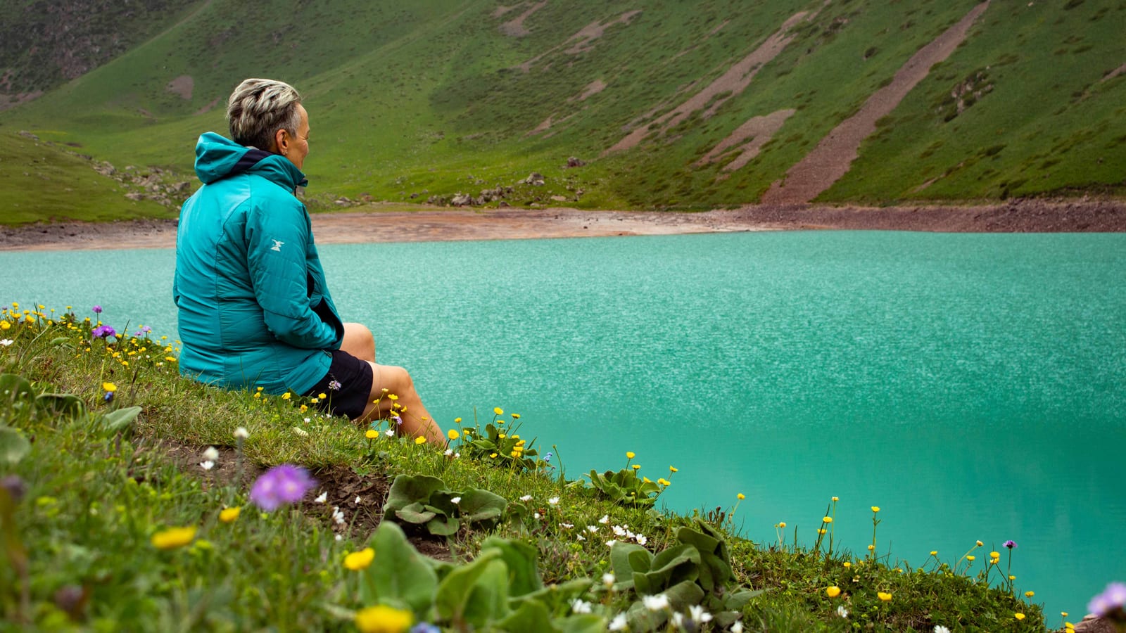 A traveller resting by a turquoise mountain lake in Kyrgyzstan